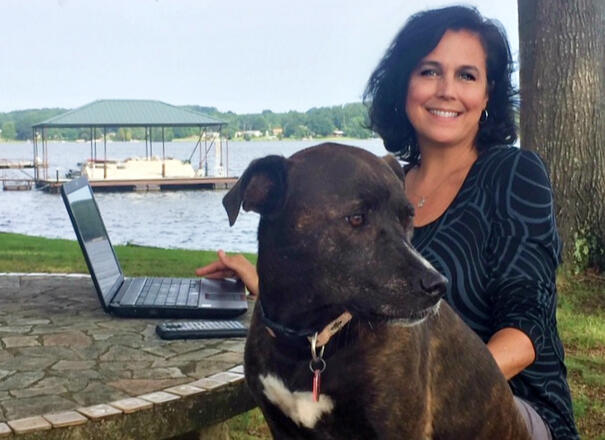 Kathy & Bella sitting by lake with laptop Lady and her dog sitting at a table by a lake. Laptop on table.